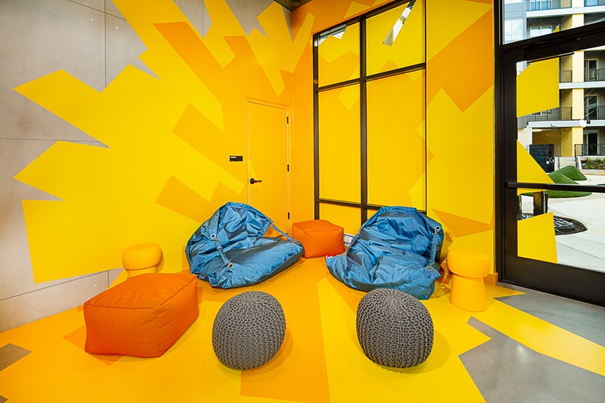 Yellow blast wall mural in lounge with bean bag and poof chairs at scout Fairfax luxury apartments