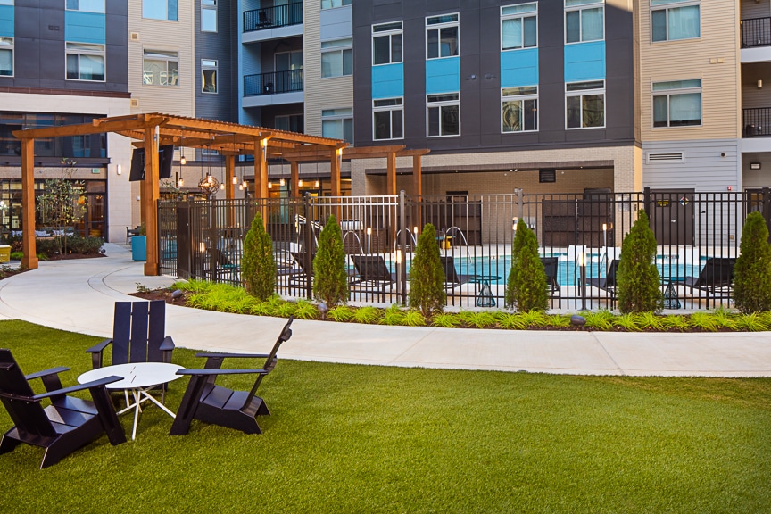 Pool deck with lush green lawn, social seating, pergola, view of pool and apartment building in background at scout Fairfax luxury apartments