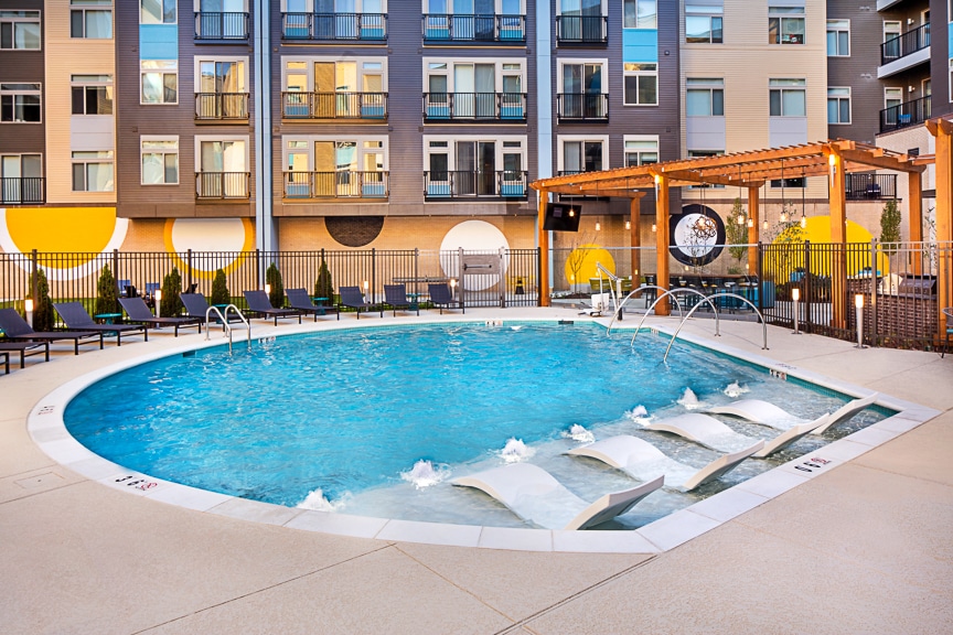 Pool with in pool chaise lounge chairs, pergola, social seating, and view of apartment building in the background at scout fairfax luxury apartments