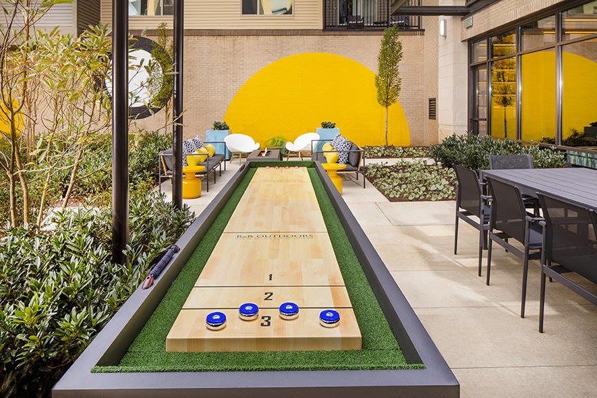 Shuffleboard table, communal dining, and social seating at the outdoor lounge at scout fairfax luxury apartments