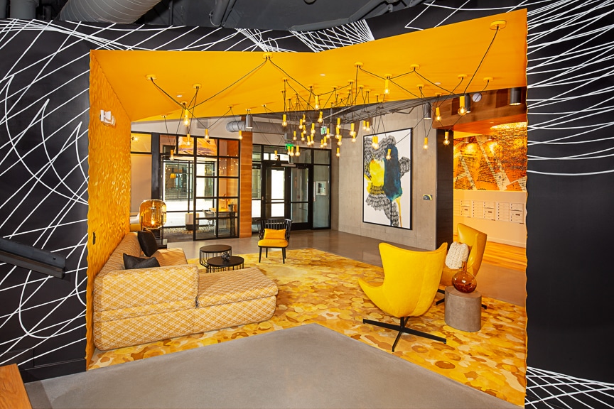 Yellow themed resident lounge with social seating, sofa, cocktail tables, and modern artwork and lighting at scout fairfax luxury apartments
