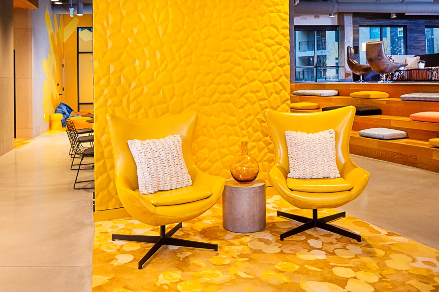 Close up of yellow leather stuffed chairs with a yellow textured wall in the background at scout fairfax luxury apartments