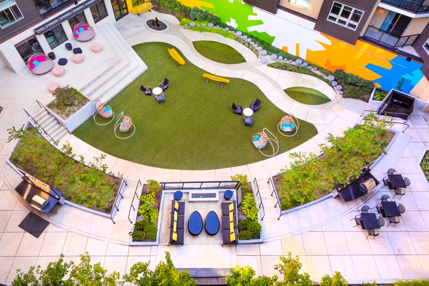 aerial view of courtyard with social seating, colorful artwork, lush green space, grill stations and views of apartment balconies at scout on the circle fairfax luxury apartments